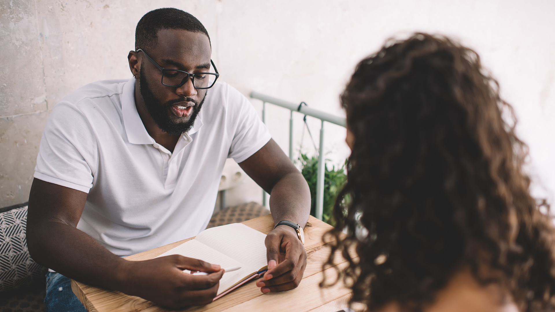 Un mentor explique quelque chose à sa mentorée, carnet ouvert sur la table